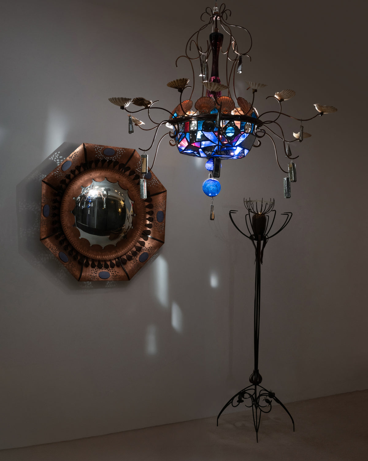 Lampadaire « Pavot » de Dubreuil dans une pièce sombre, avec le lustre à verres bleus éclairé et le miroir sorcière en cuivre