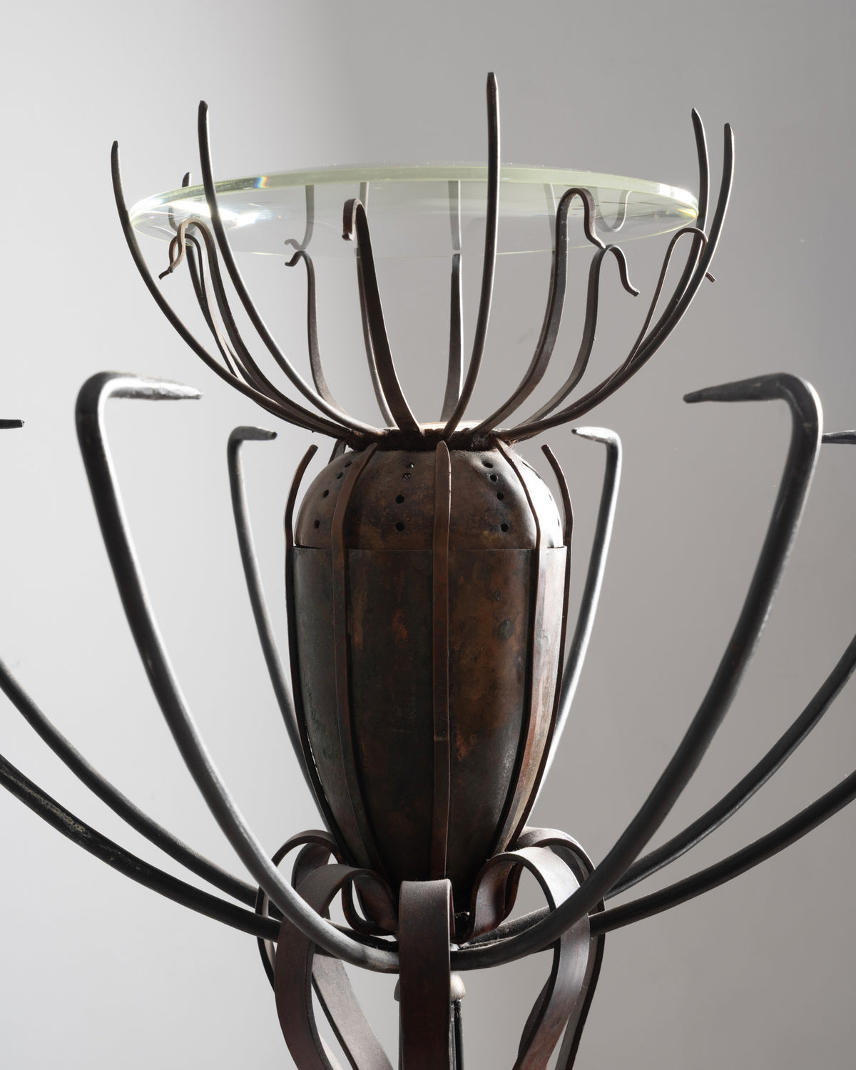 Gros plan sur la tête du lampadaire « Pavot » de Dubreuil : capsule en cuivre perforée, tiges et coupe en verre